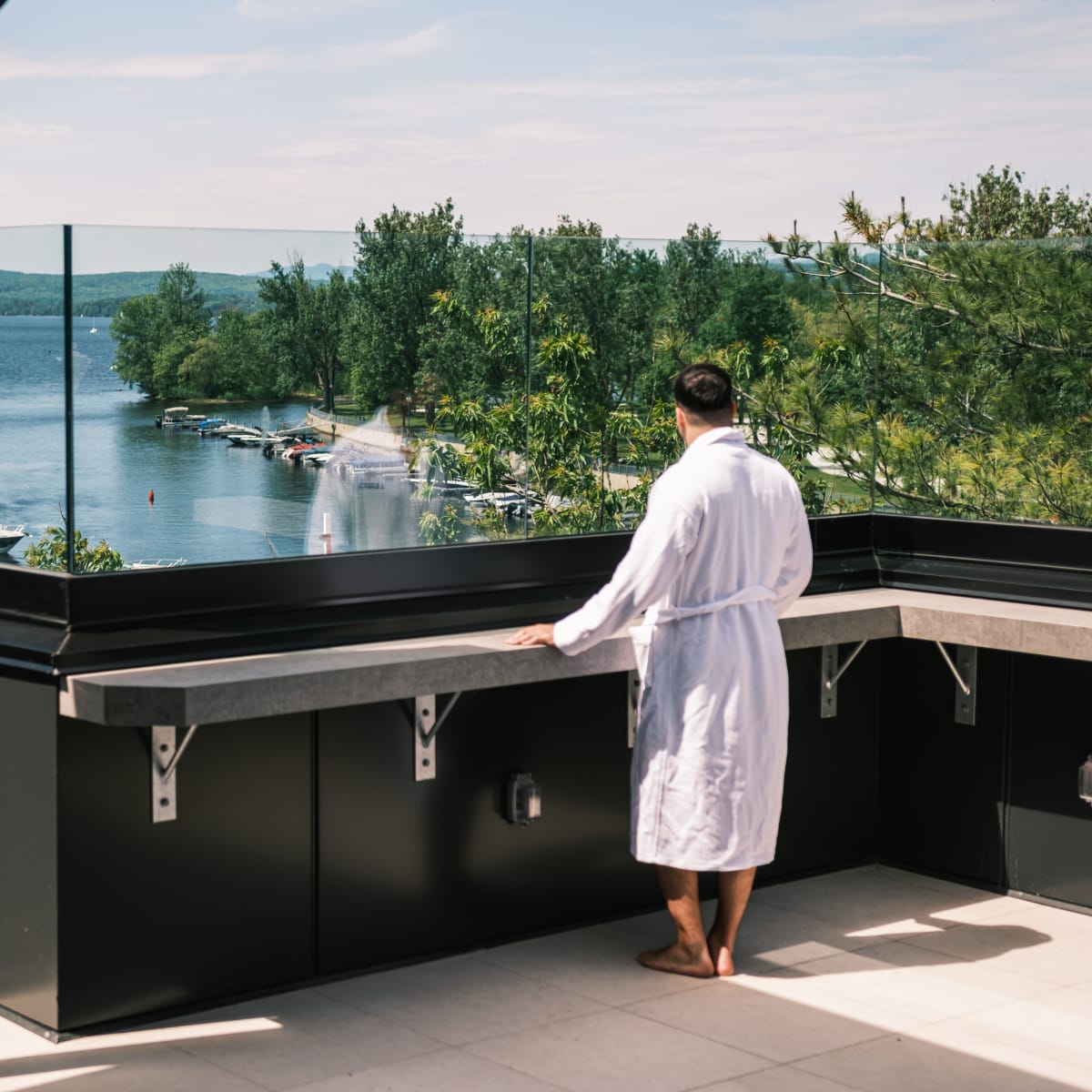 Man in a bathrobe on a balcony looking at the lake.