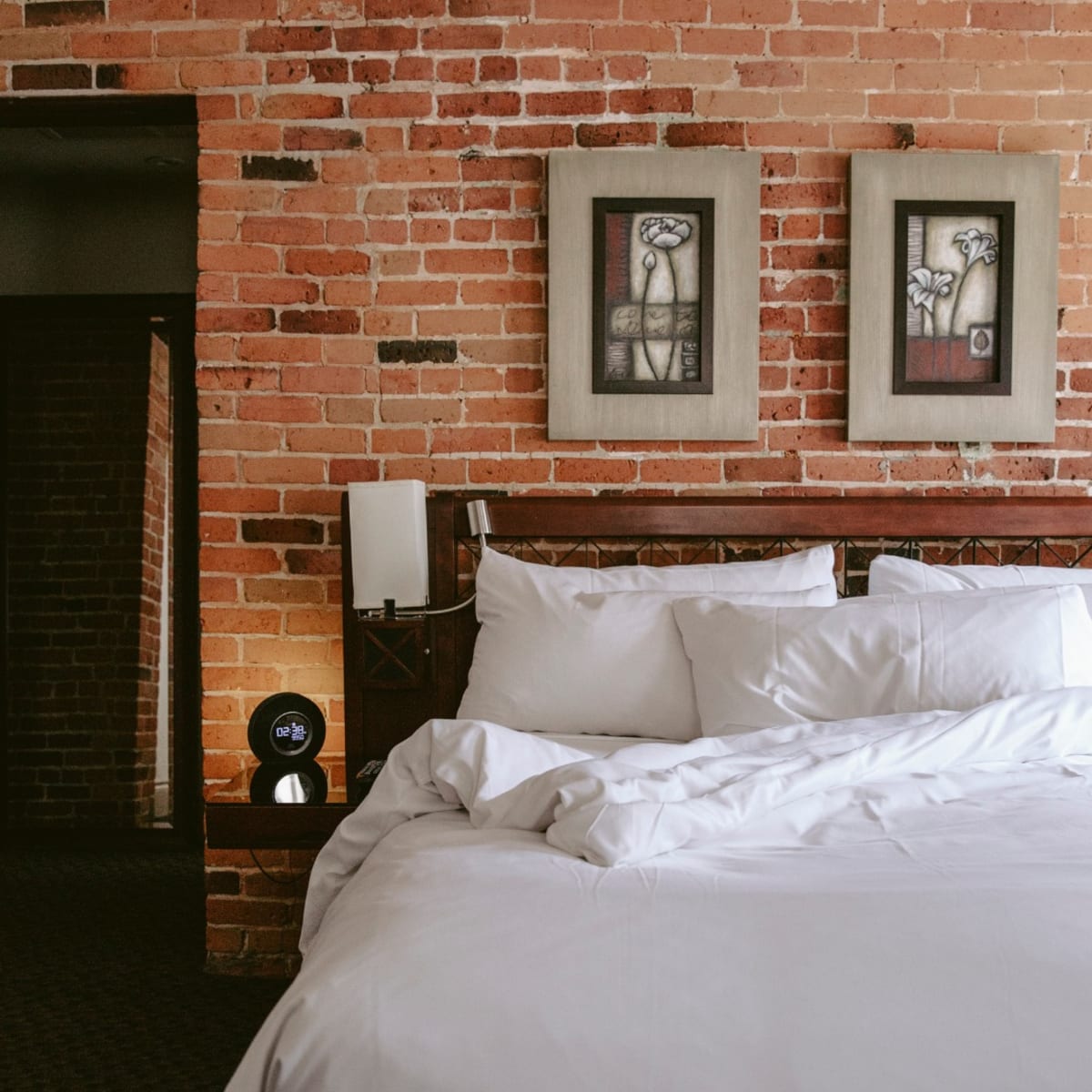 Hôtel Nelligan - A bed with white linens and a brick wall