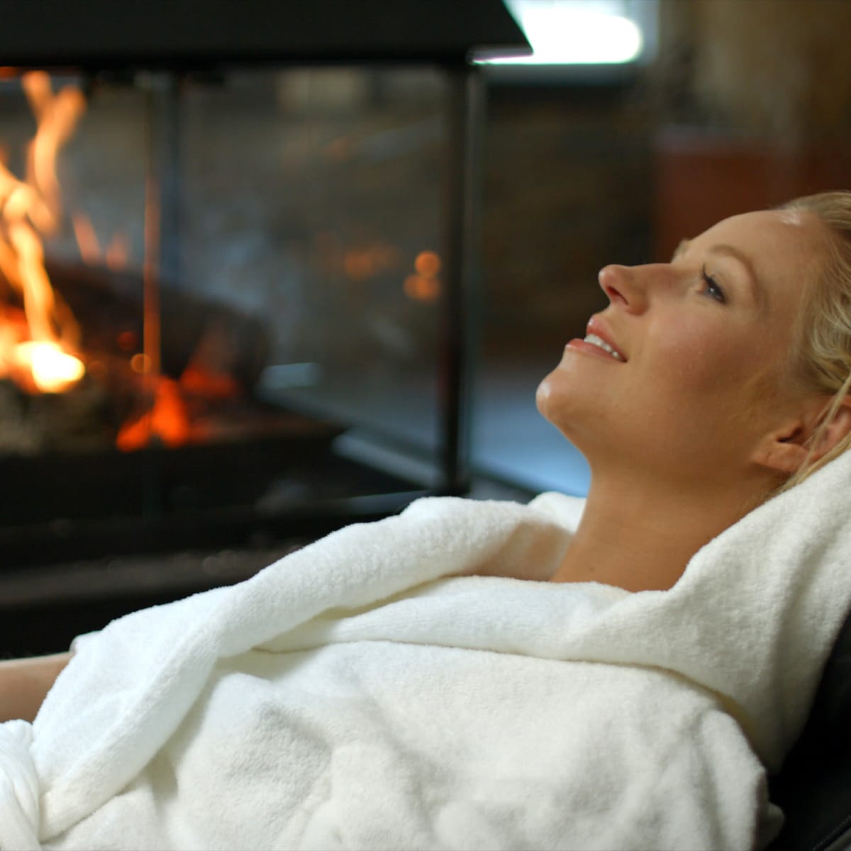 Femme en peignoir en train de se détendre à proximité d'un feu de foyer.