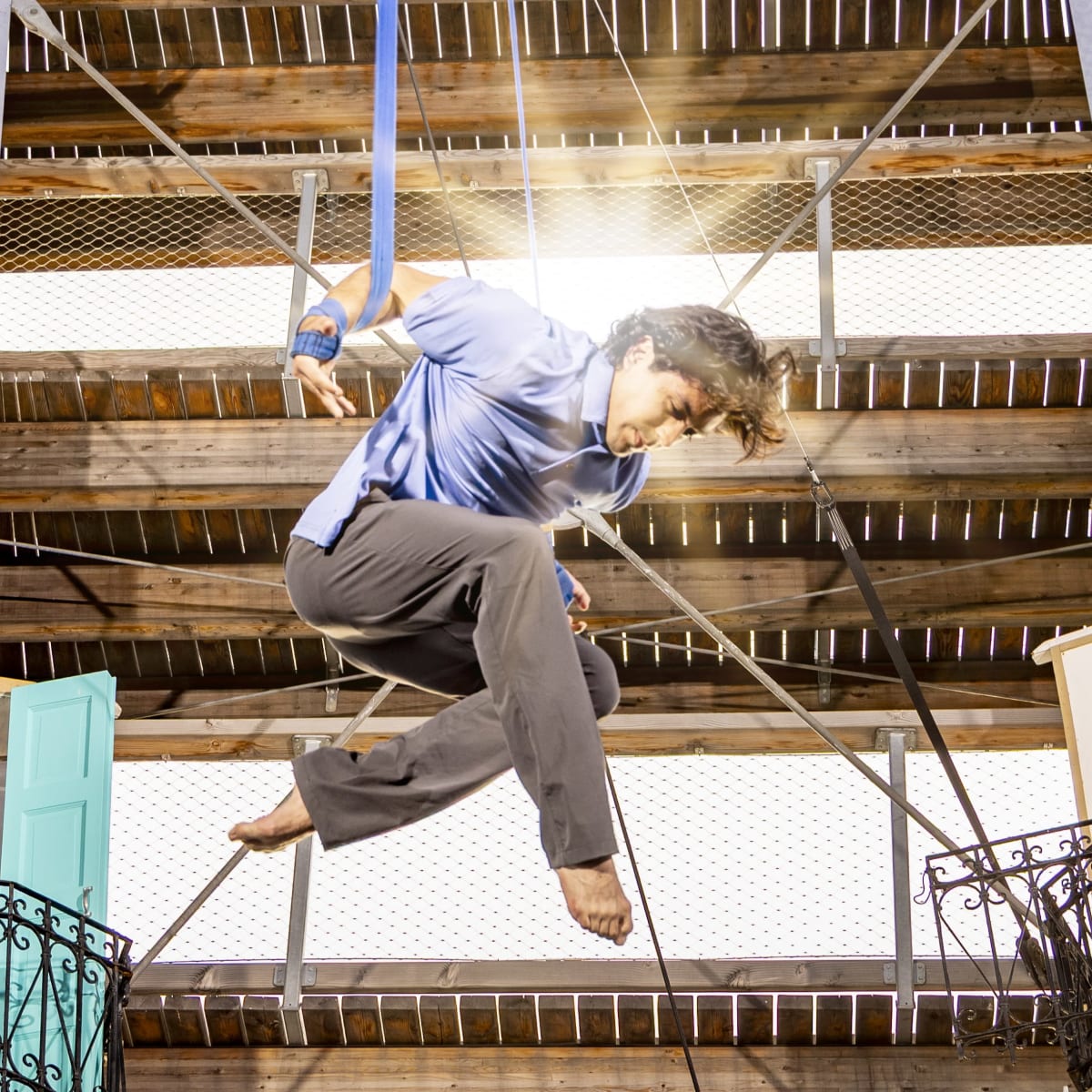 An acrobat suspended in front of rays of sunlight. 