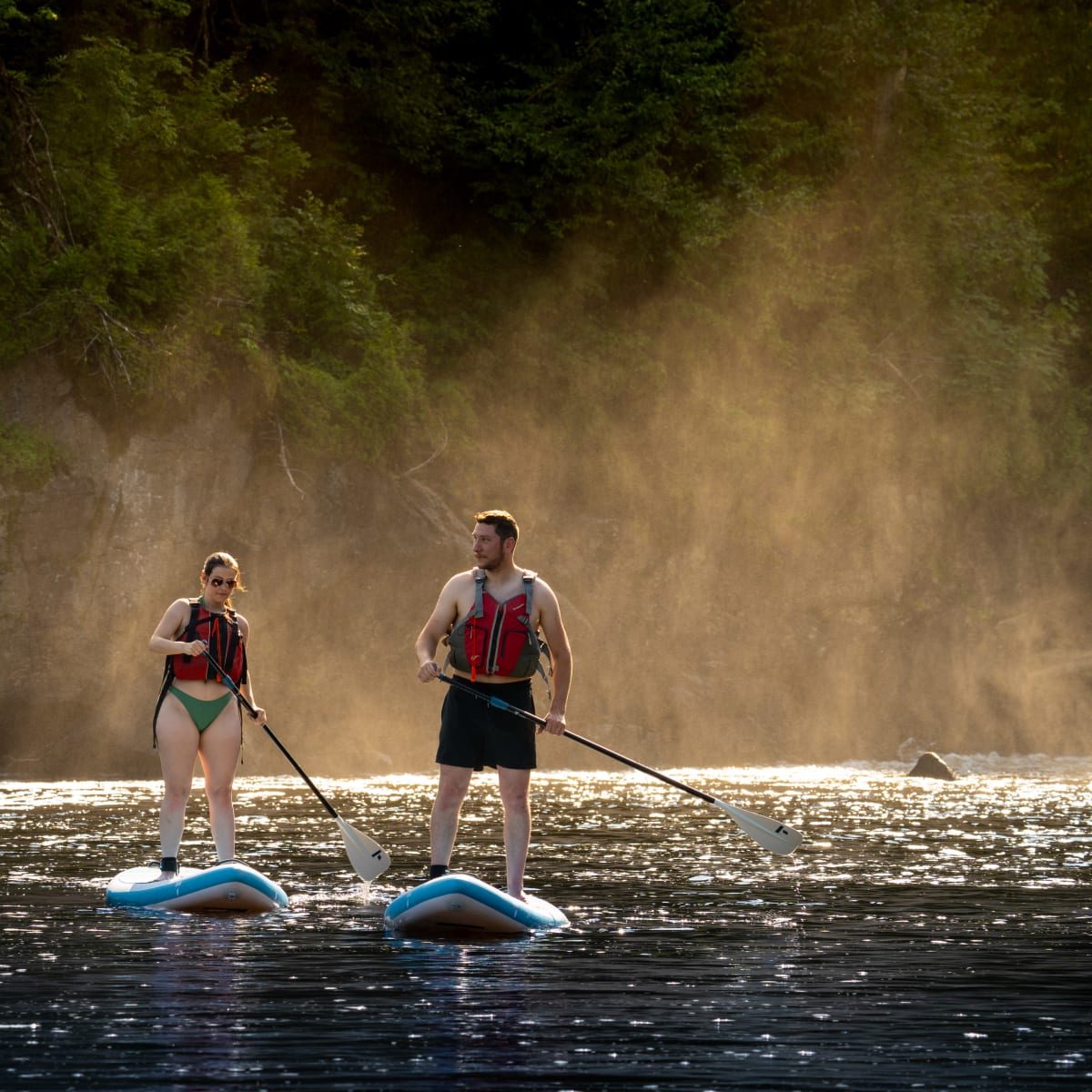 A man and a woman standing on two stand-up paddleboards, wearing life jackets.
