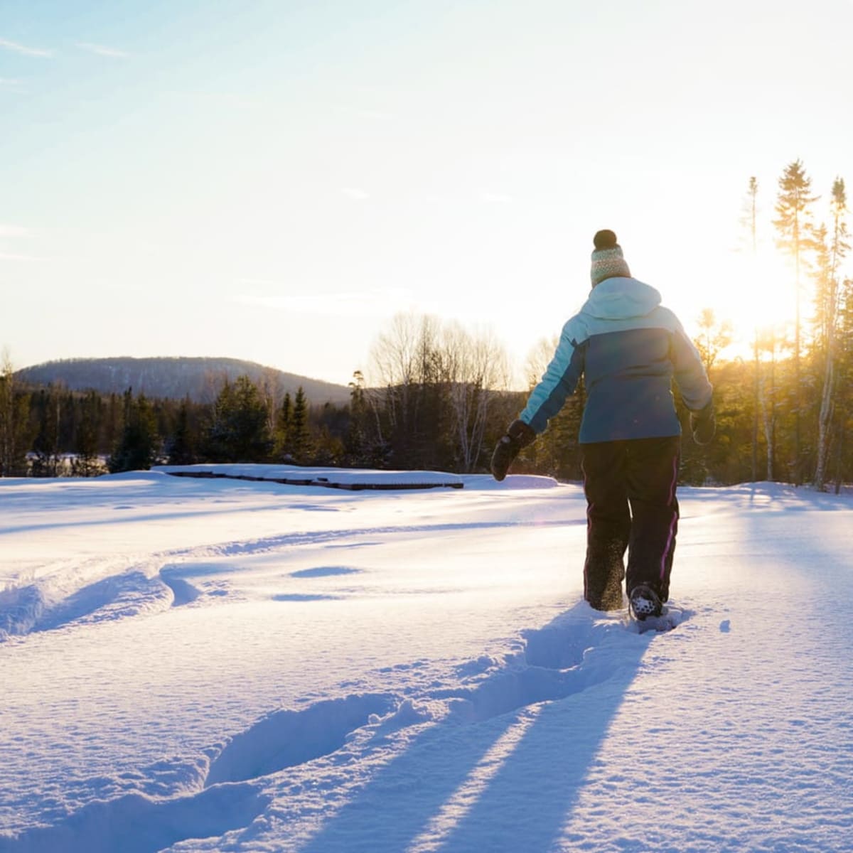 Person walking in a snowy landscape, under a very sunny sky.
