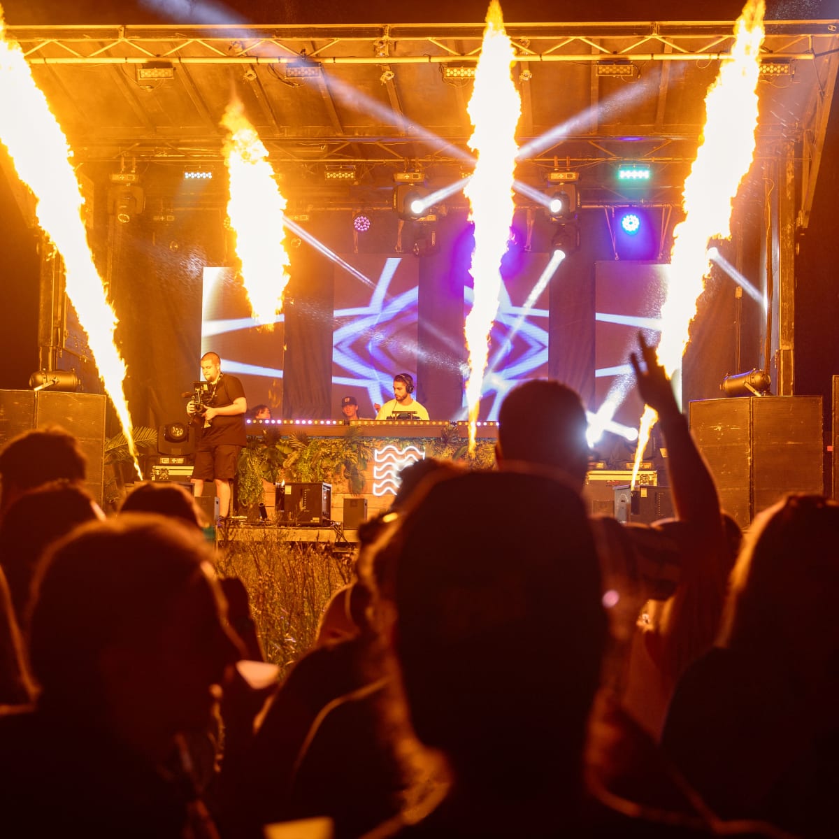 M DGTL - Un DJ est sur scène pendant la nuit, éclairé par des projecteurs de flammes.
