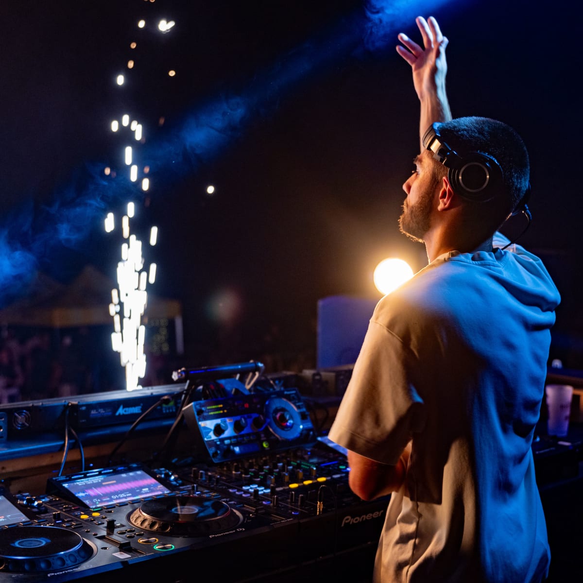 M DGTL - Un DJ se tient devant son équipement, la main vers le ciel.