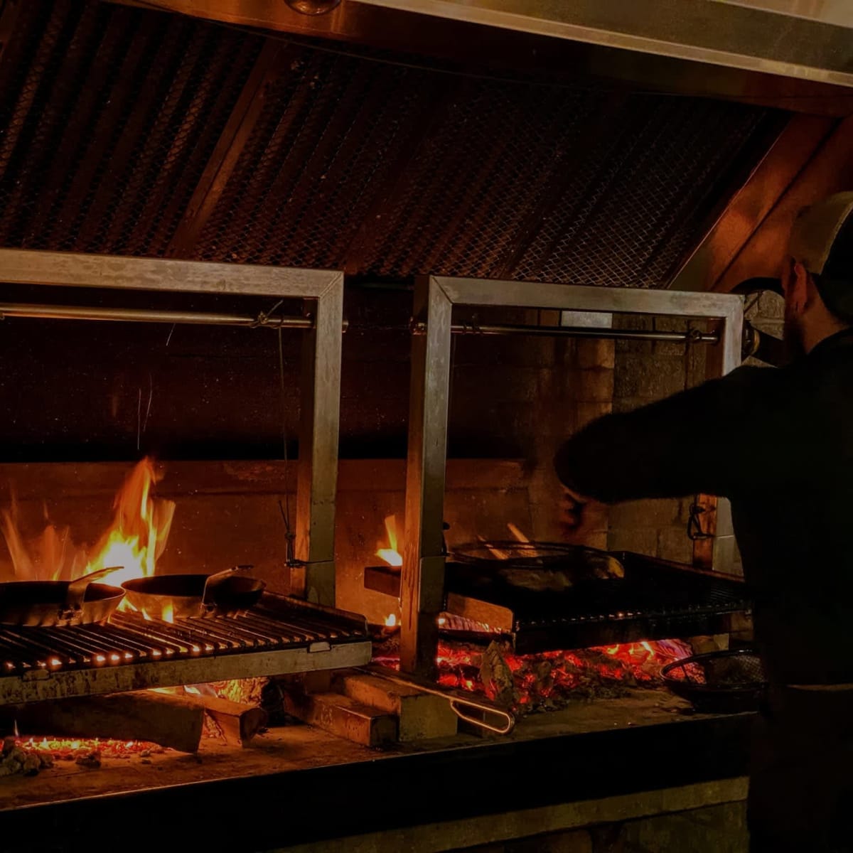 A cook preparing food over hot coals. 