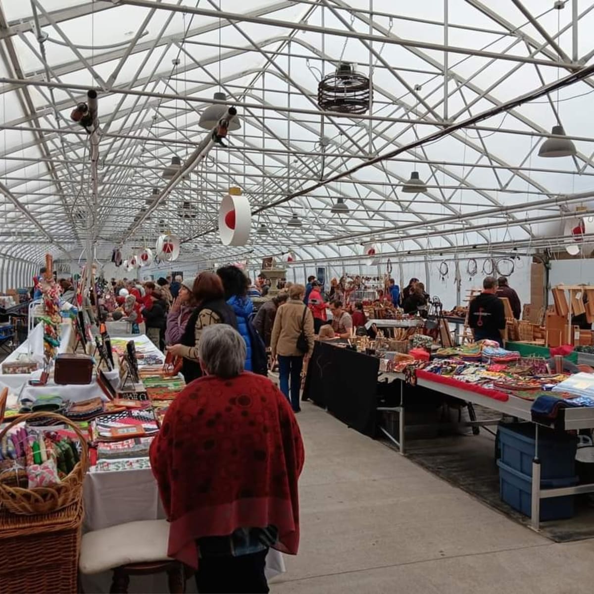 Artisan market set up in a large greenhouse, filled with visitors and colorful stalls.