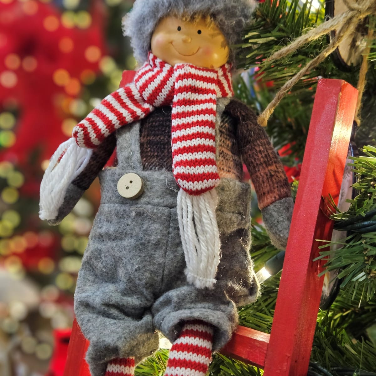Smiling elf figurine in winter clothing hanging on a decorated Christmas tree.