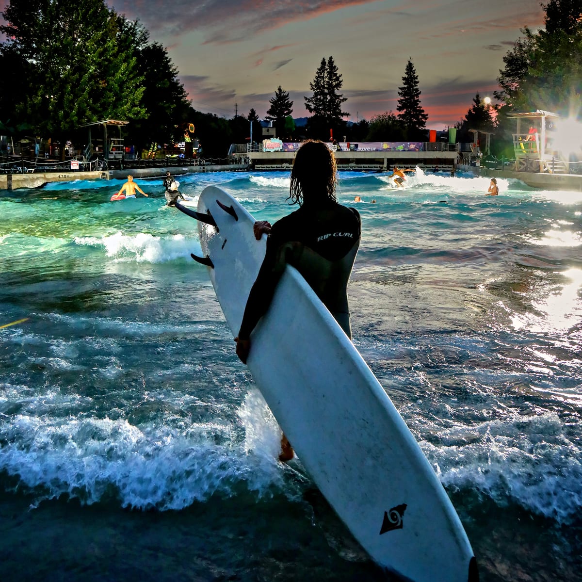 Surfeur.se sur le bord de la piscine à vagues en soirée.