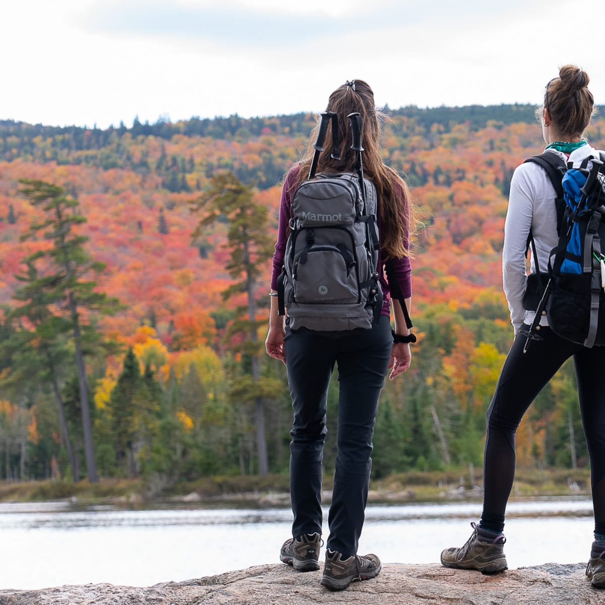 2 femmes avec des sacs de randonnées regardent la vue d'un lac.