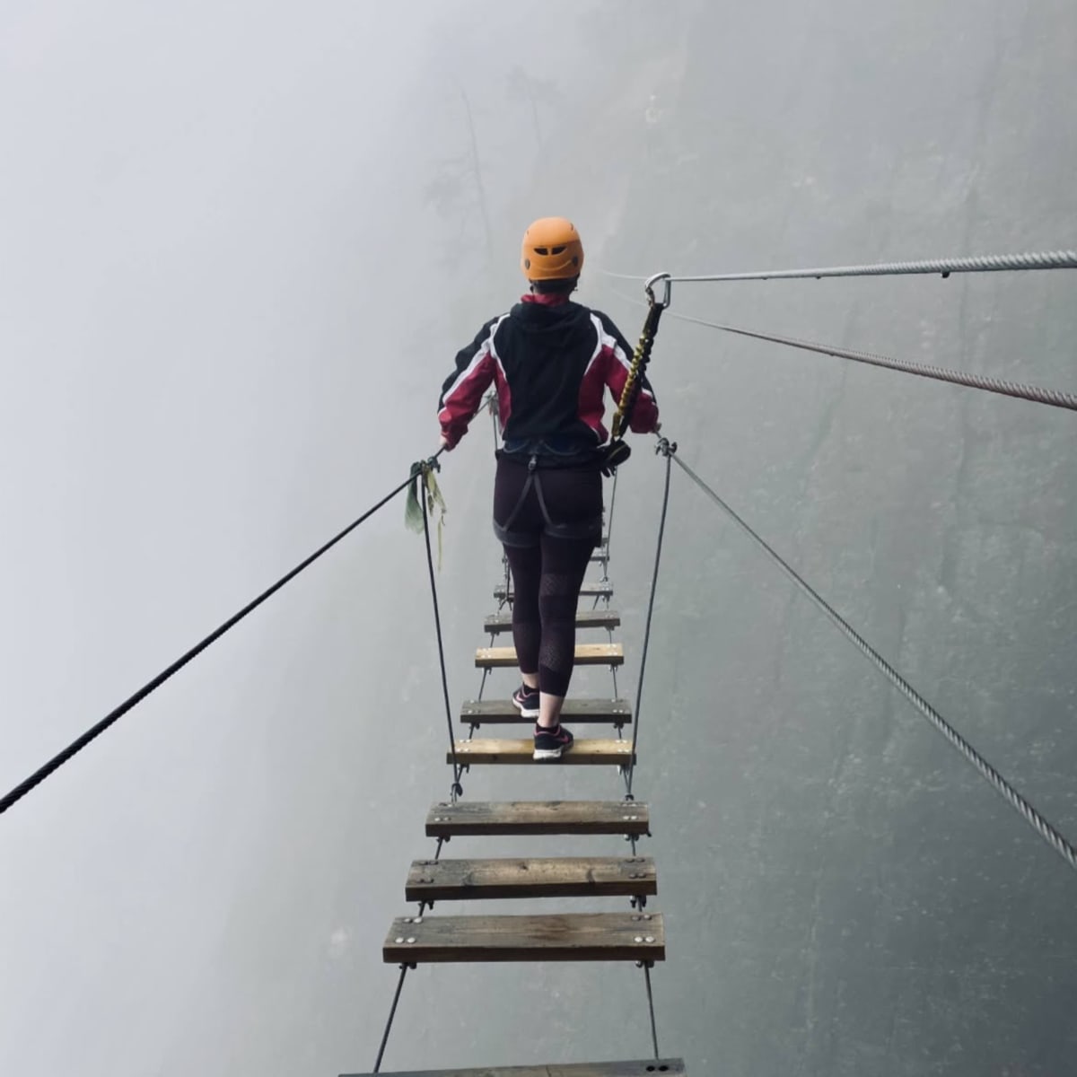 A woman on a suspension bridge on a via ferrata in foggy weather..