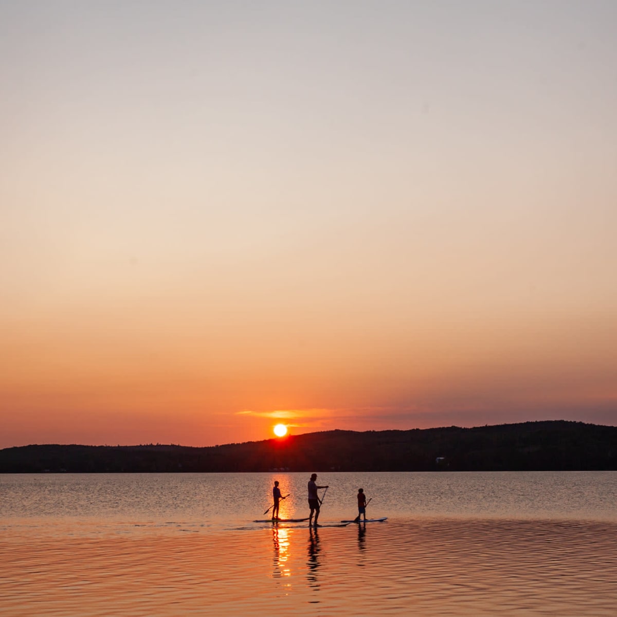 Trois personnes en planche à pagaie au coucher du soleil à la plage de Haldimand.