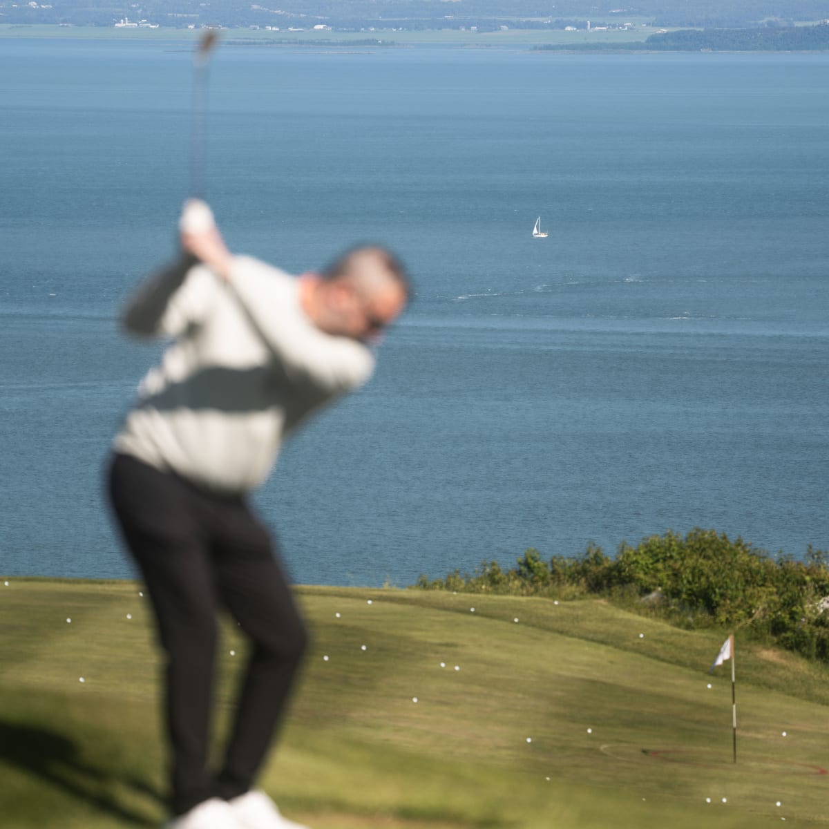 Golfeur en train de s'élancer au Golf Manoir Richelieu; le focus est sur le fleuve en arrière-plan plutôt que sur l'homme.