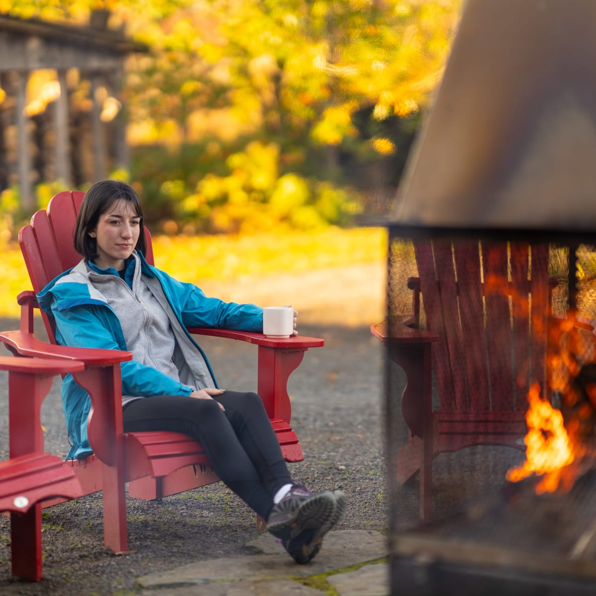 Femme relaxant devant un feu extérieur à l'automne.