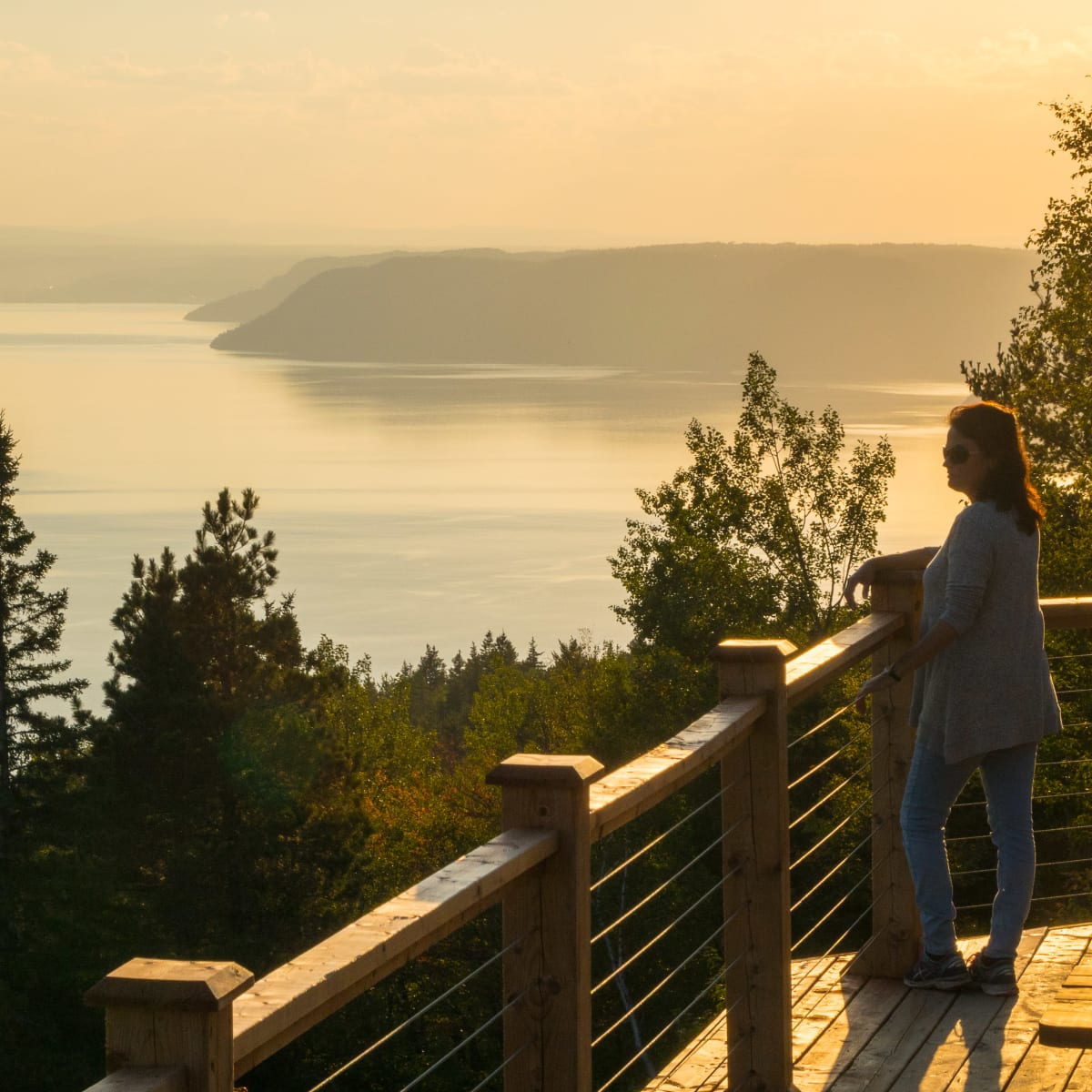 A woman looking out at a panoramic view of the fjord at sunset.
