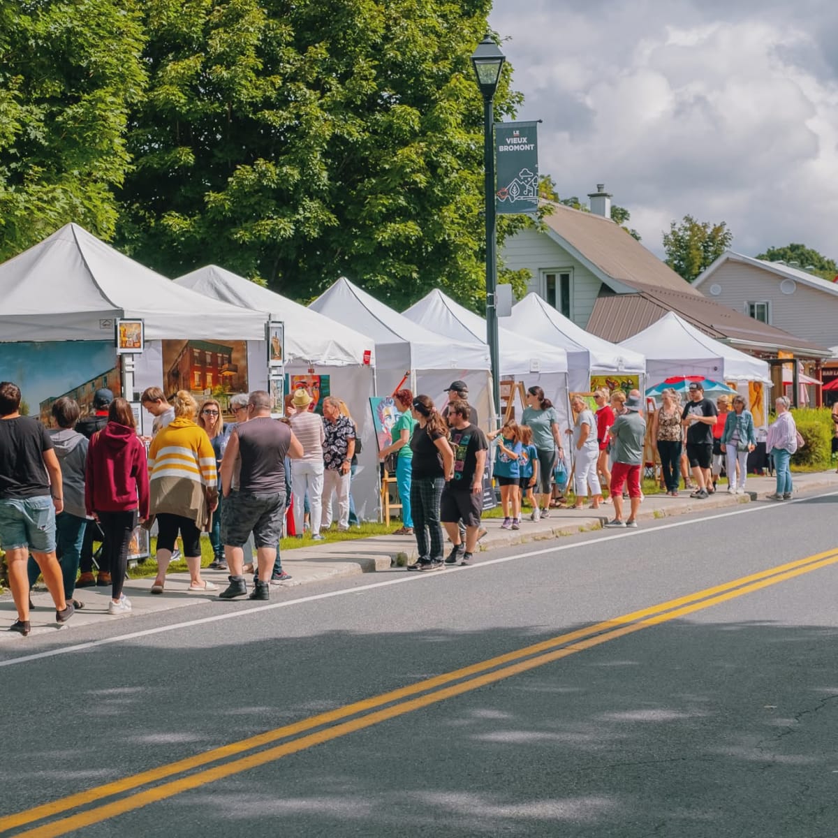 Rows of outdoor booths at the Bromont Art Symposium; many people are visiting each of the booths.