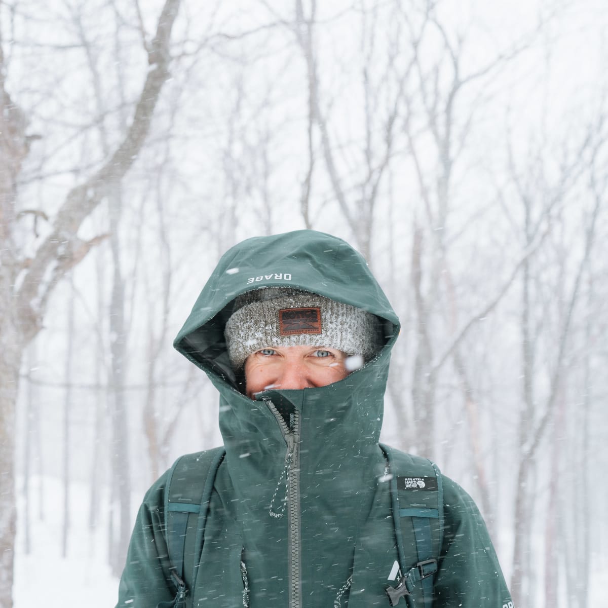 Woman wrapped up in a green coat in the middle of a snowy landscape.