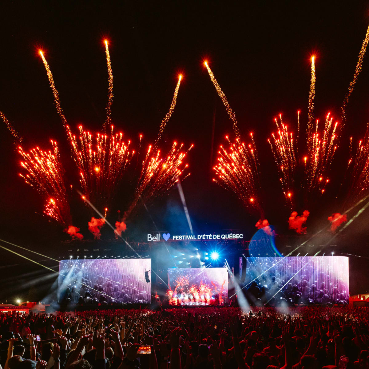 Crowd in front of an outdoor stage at night with fireworks.