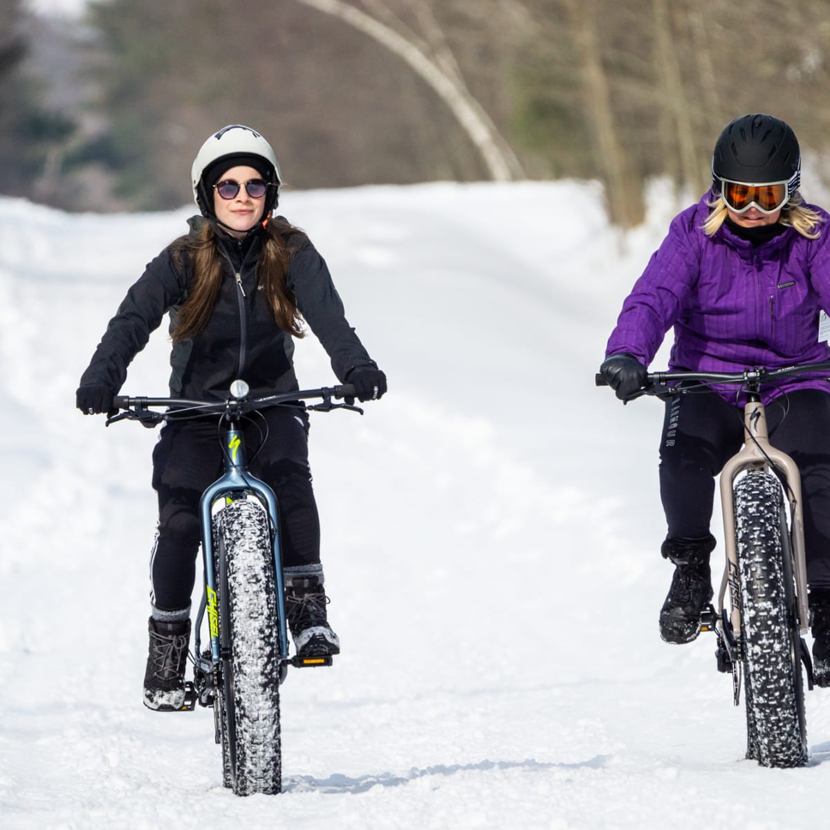 Two women on fatbikes on a snow-covered but clear trail.