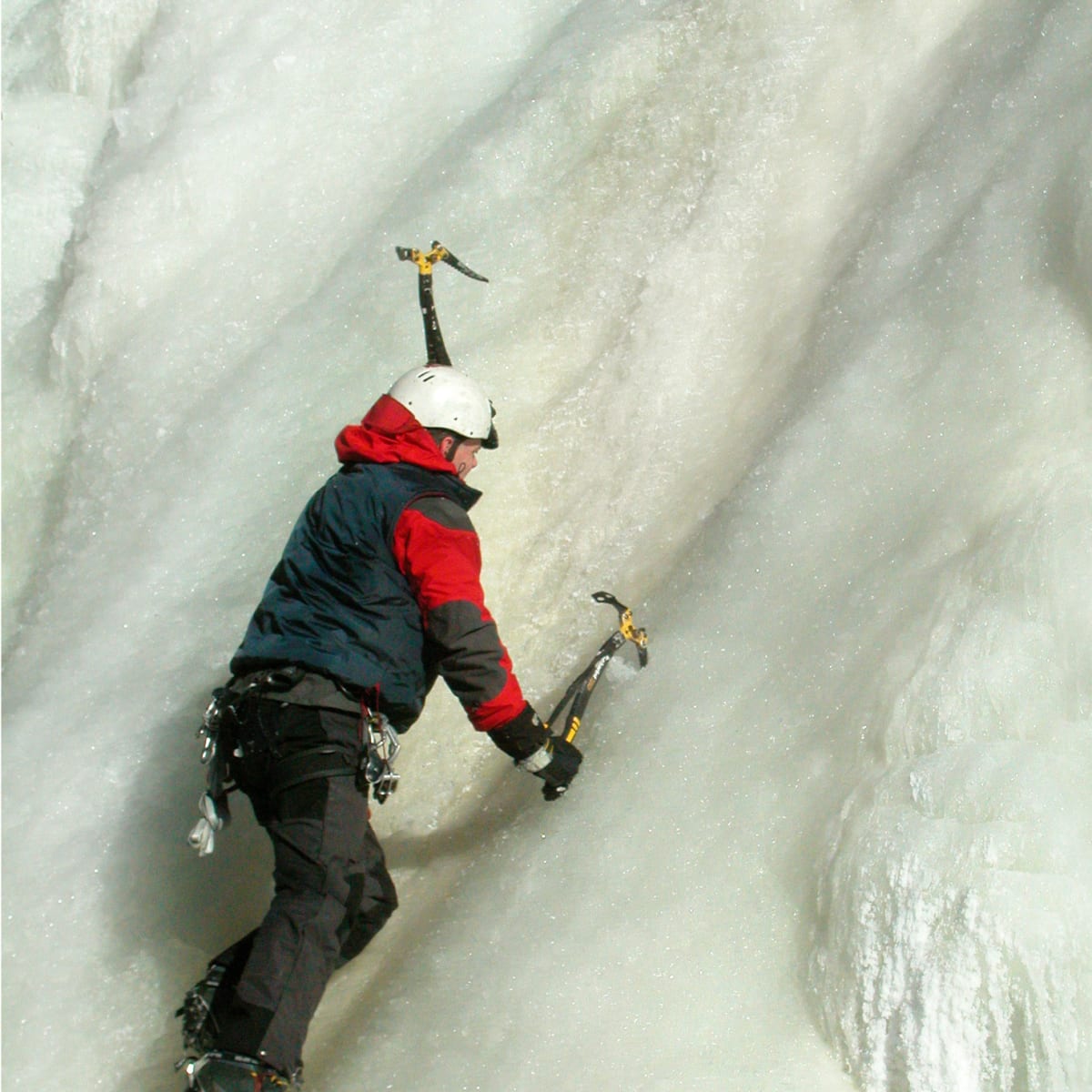 Close-up shot of a climber with ice axes in his hands, climbing an ice wall.