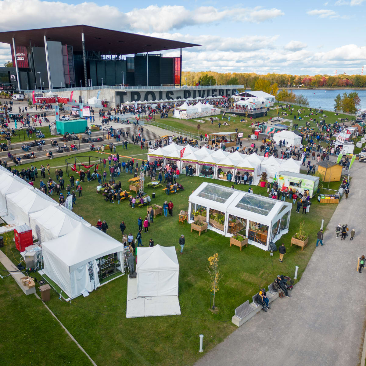 The Amphithéatre Cogeco in Trois-Rivières by the river, with kiosks and spectators on the grass.