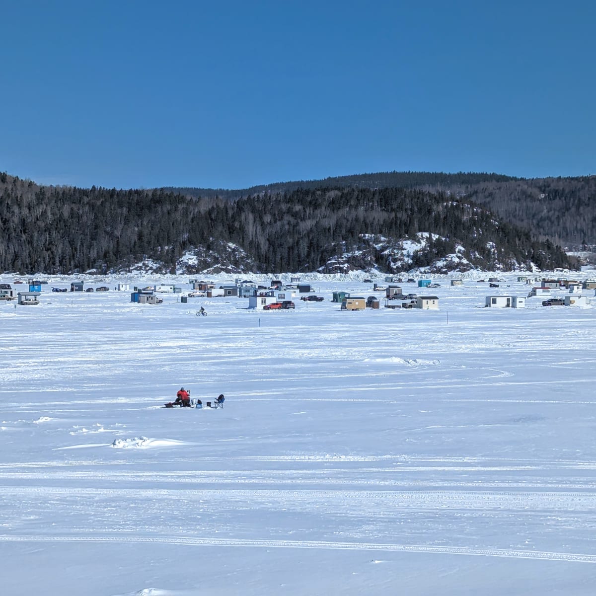 The snow-covered Saguenay Fjord and ice fishing cabins seen in the distance.