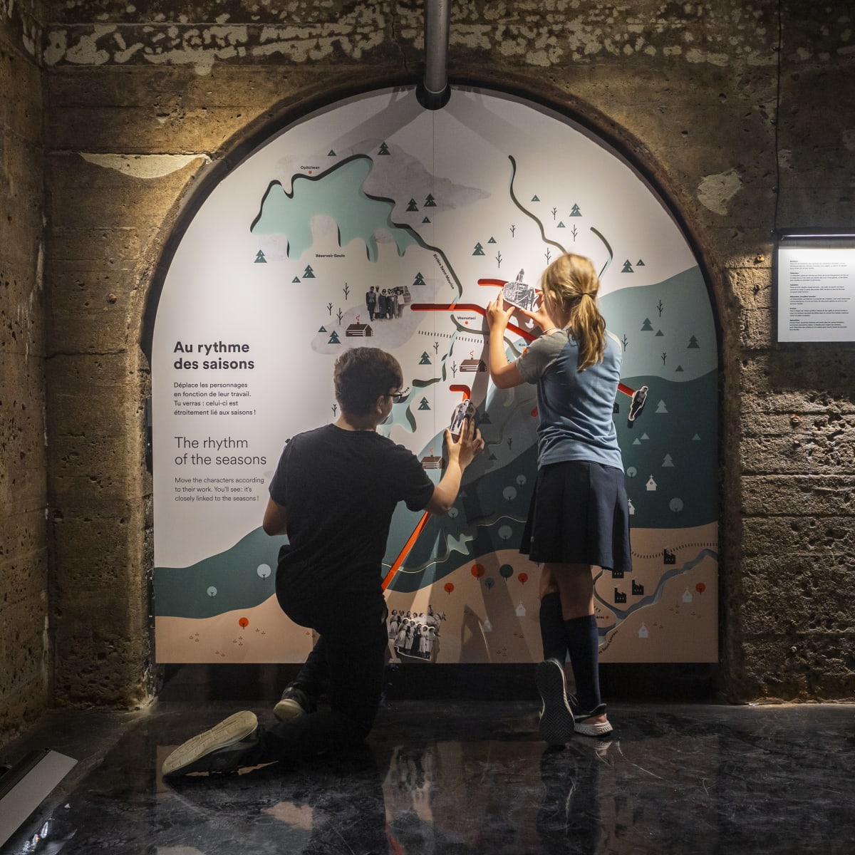 Two young people in front of an exhibition panel in a concrete room.