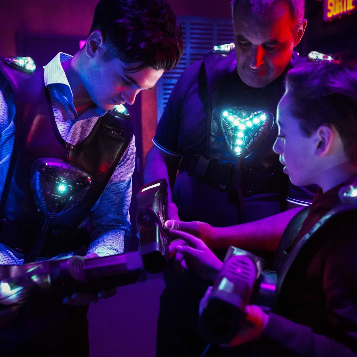 Three people wearing laser tag uniforms in a huddle.