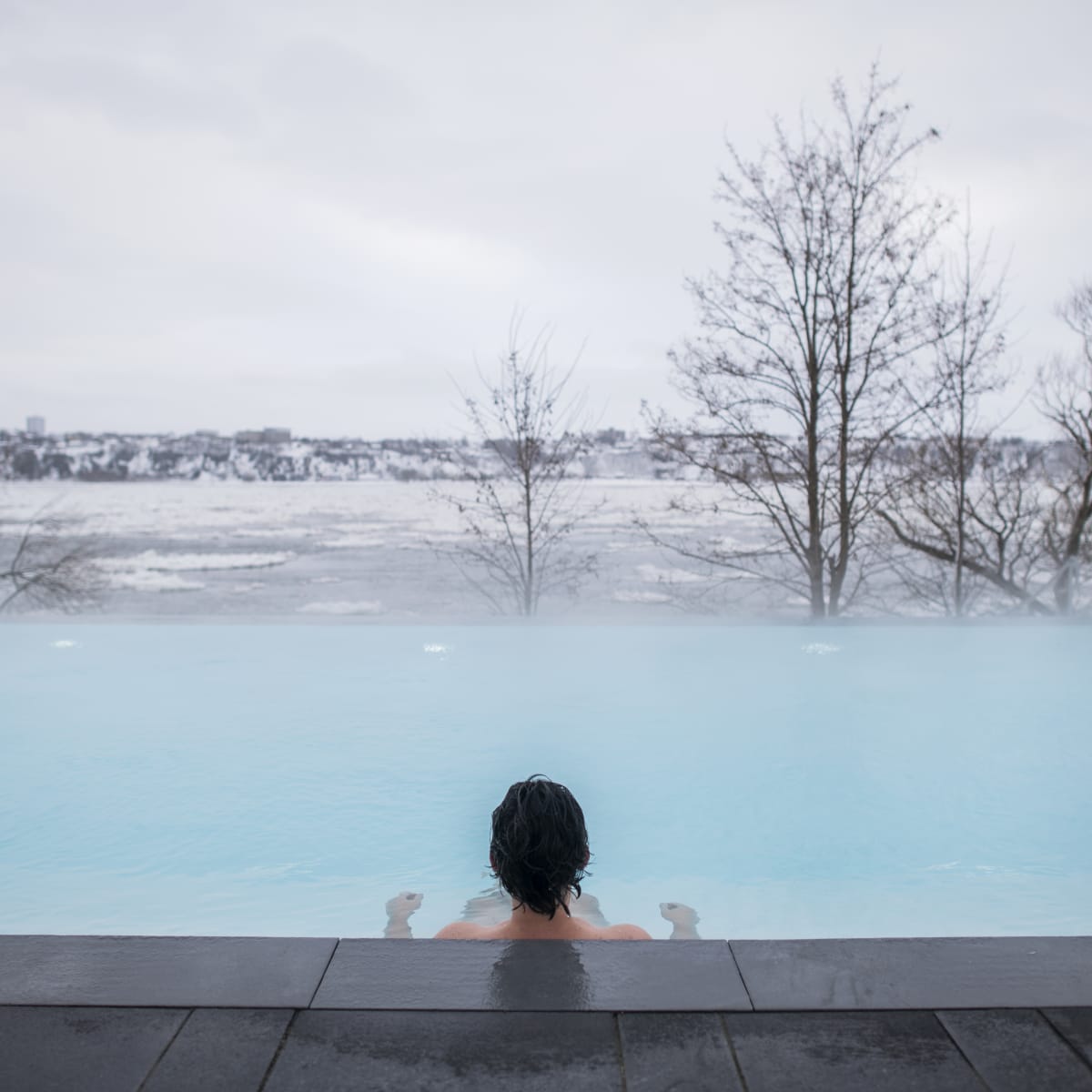 Person in a spa seen from behind as they look out over the St. Lawrence River in winter.