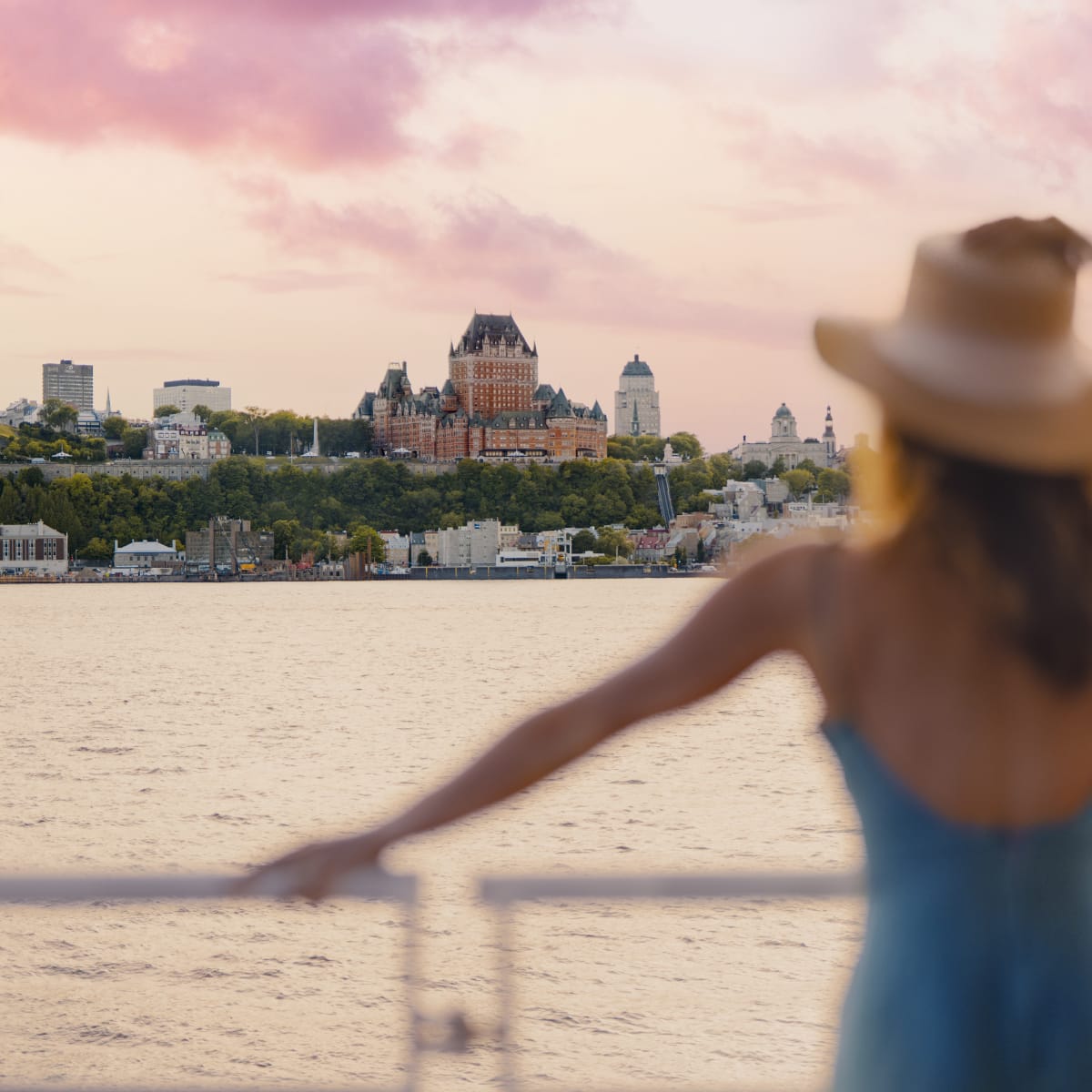A woman in a blue dress and a large hat looks out over the Château Frontenac from the St. Lawrence River.