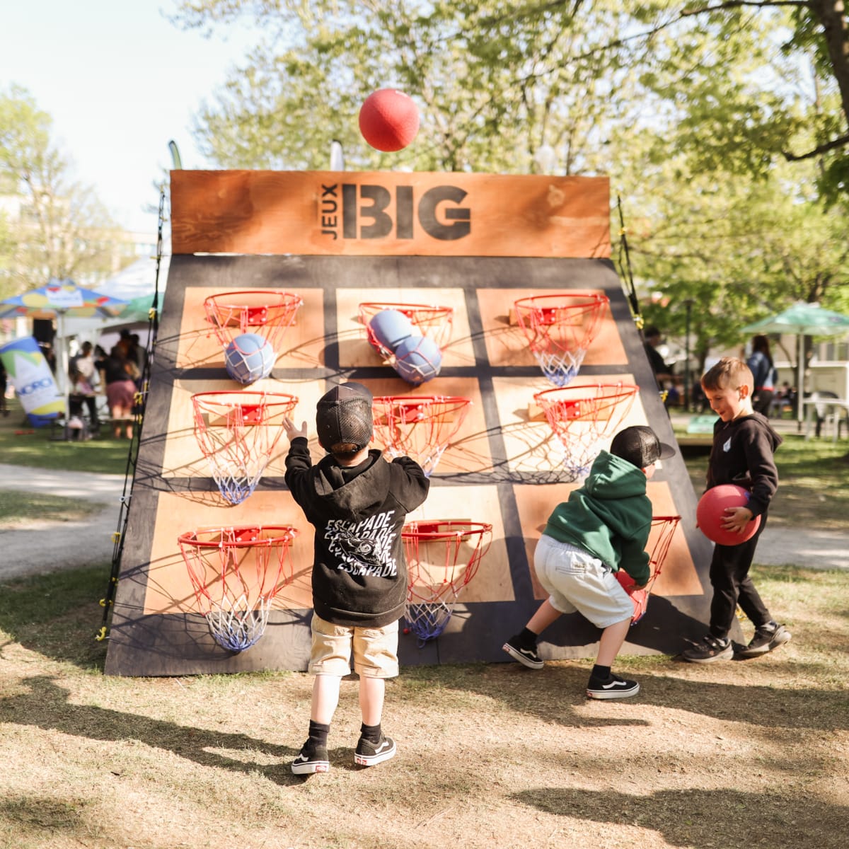 Children playing a giant game combining cornhole and basketball.