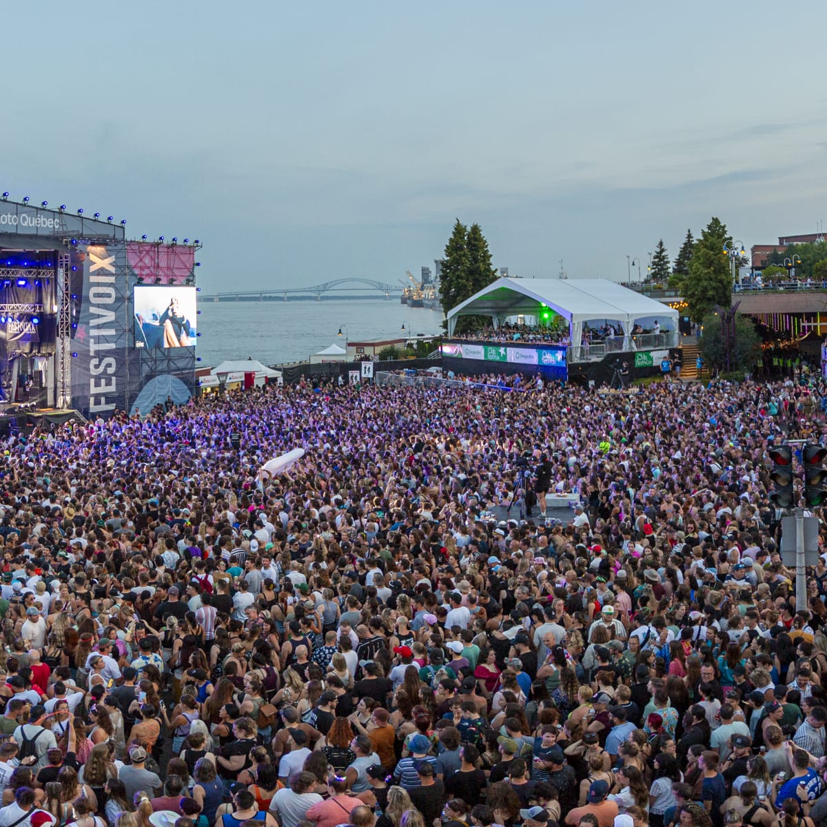A dense crowd in front of a stage by the St. Lawrence River.