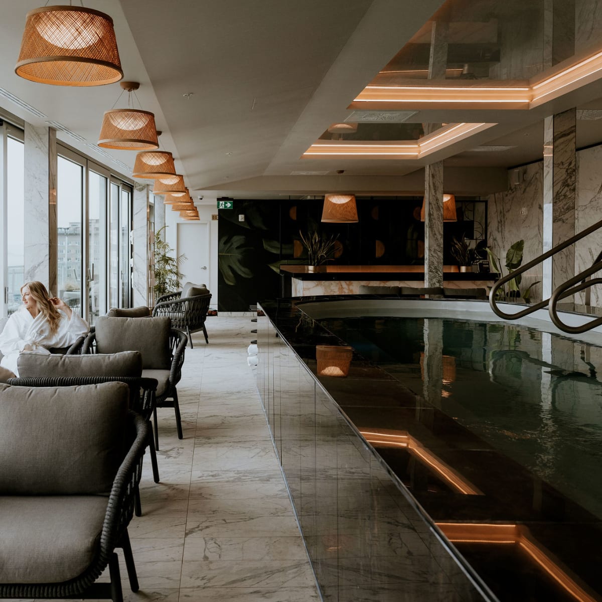 Deux personnes en peignoir assises près d’une piscine intérieure à l’ambiance zen; ils admirent la vue extérieure.