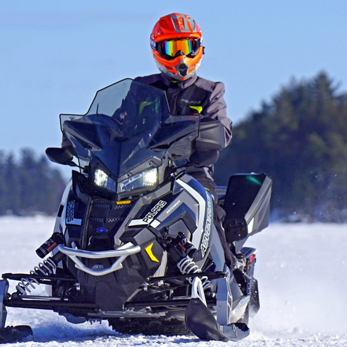 Snowmobiler on a snowmobile on the snow with a forest behind.
