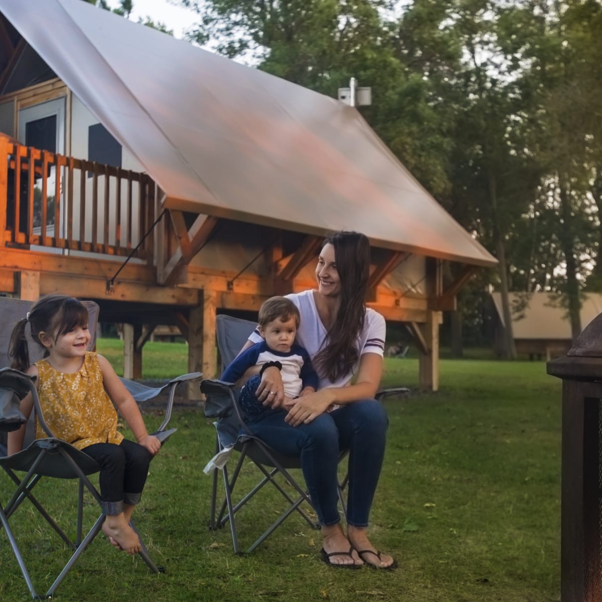 Mother and two children beside the campfire in front of a ready-to-camp unit