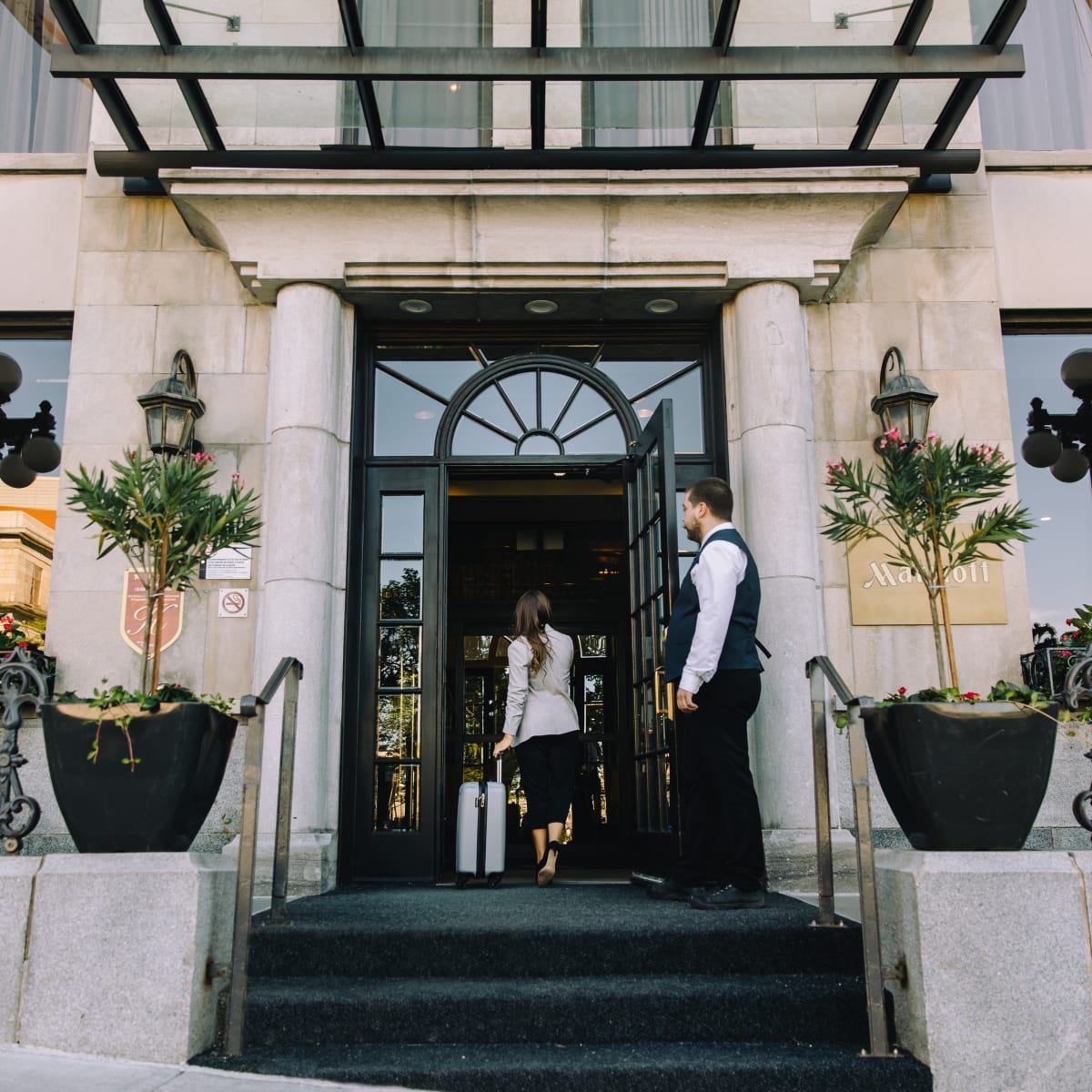 The front of a hotel; a woman walks through the door beside a doorman.