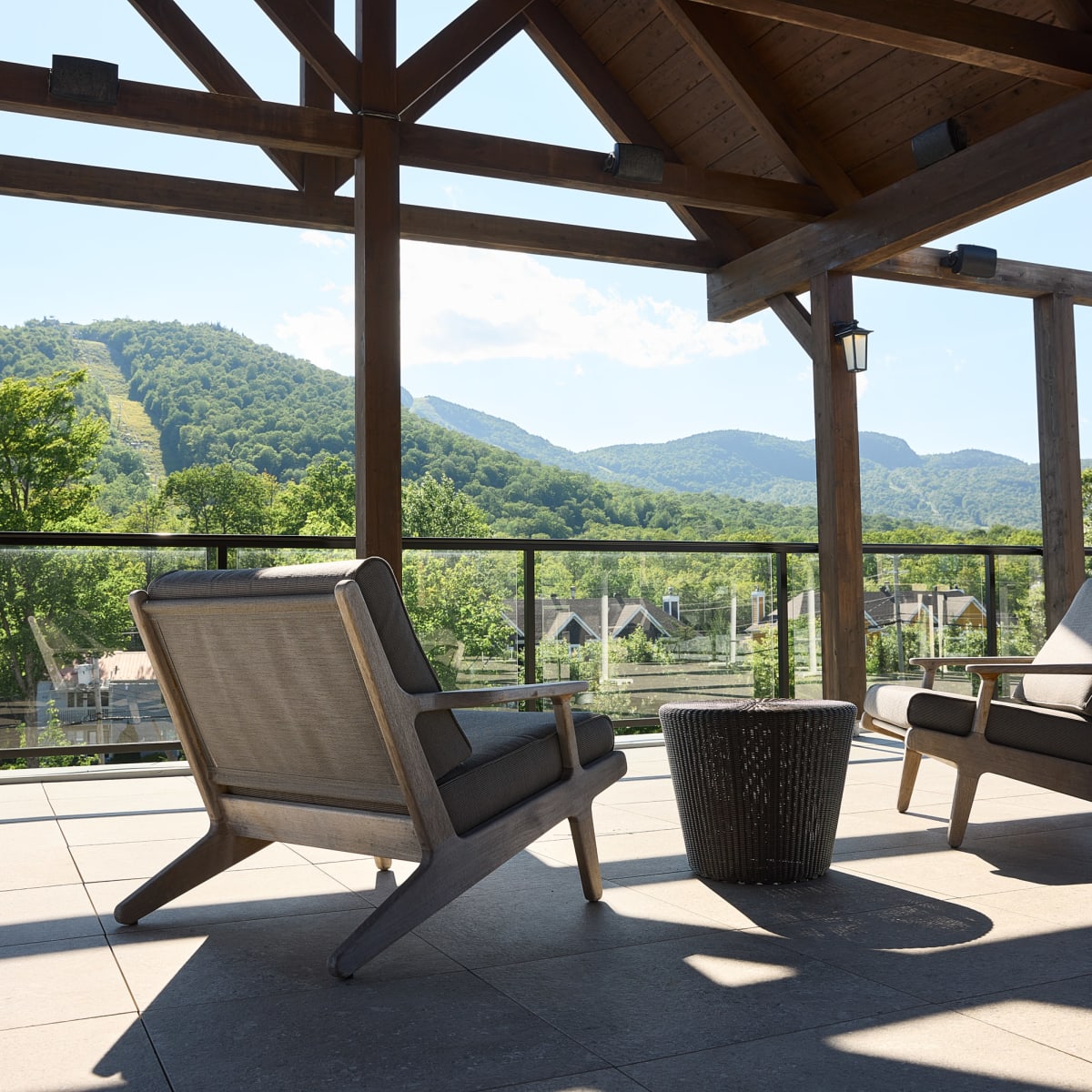 A covered outdoor terrace, featuring two comfortable chairs, overlooks a mountainous landscape.