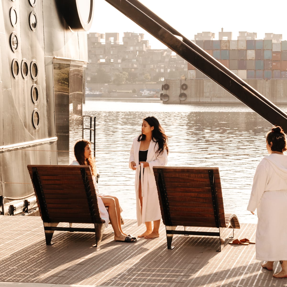 Three women in bathrobes on the spa terrace overlooking the water.