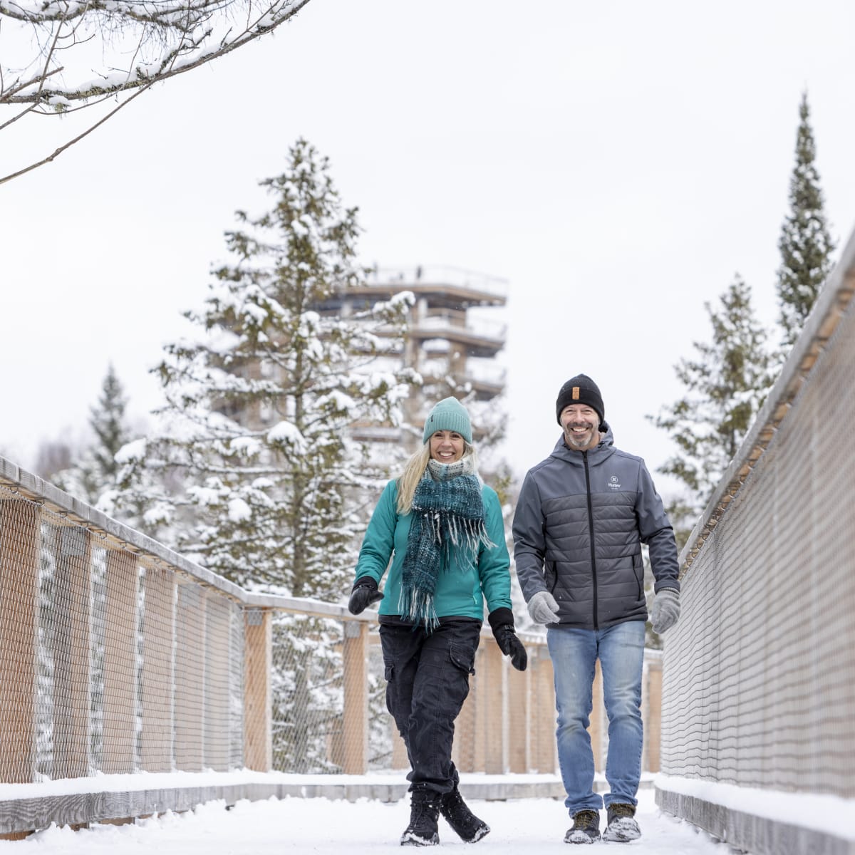 Couple souriant sur une promenage en bois enneigée.