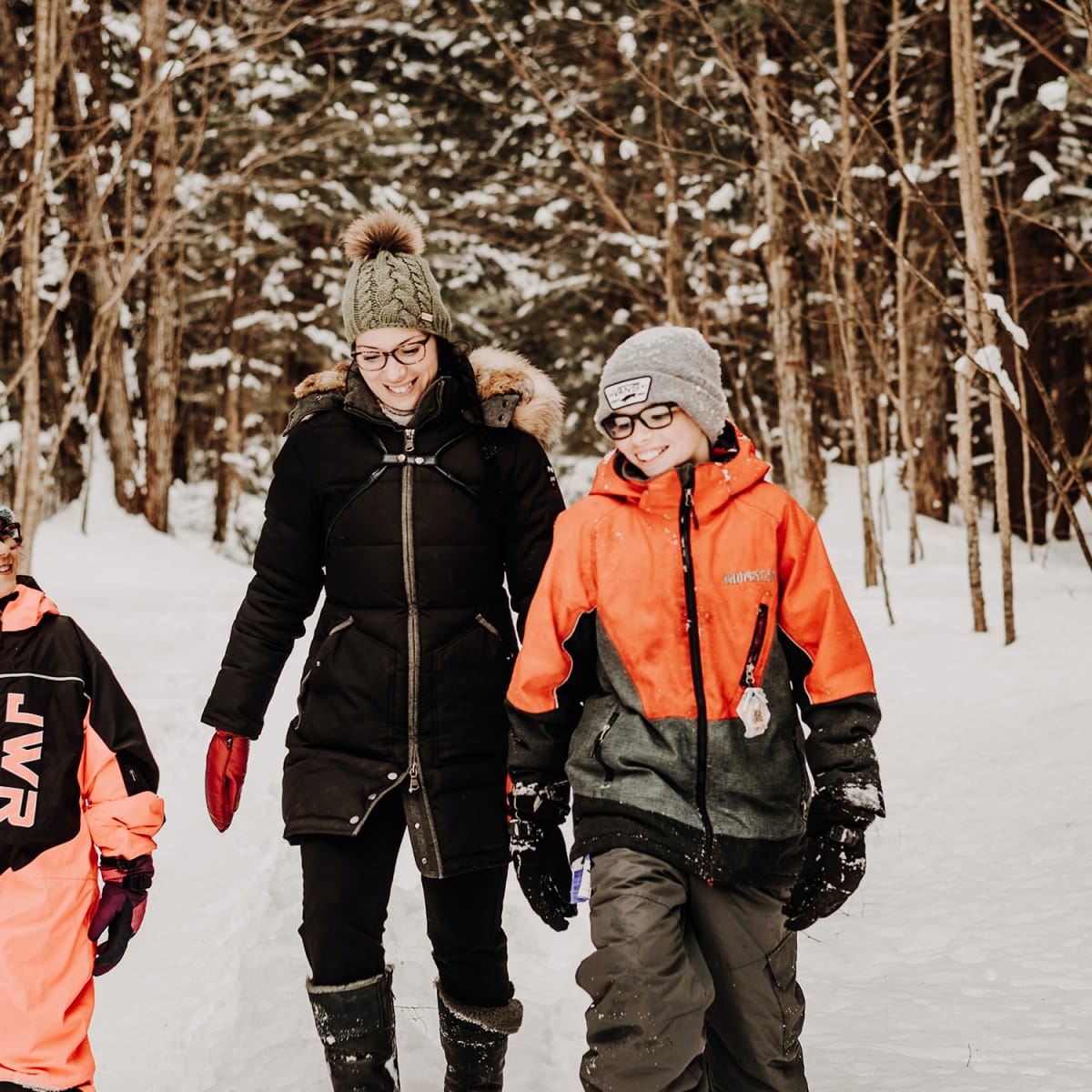 A mother and two children, all smiling, in a snowy forest.