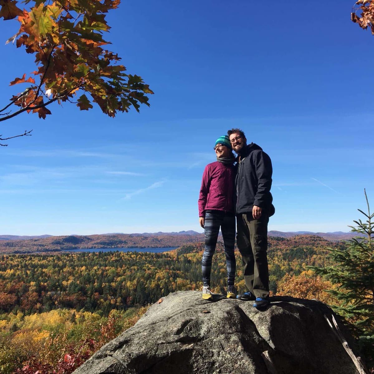 Two people posing on a rock in front of a fall landscape.