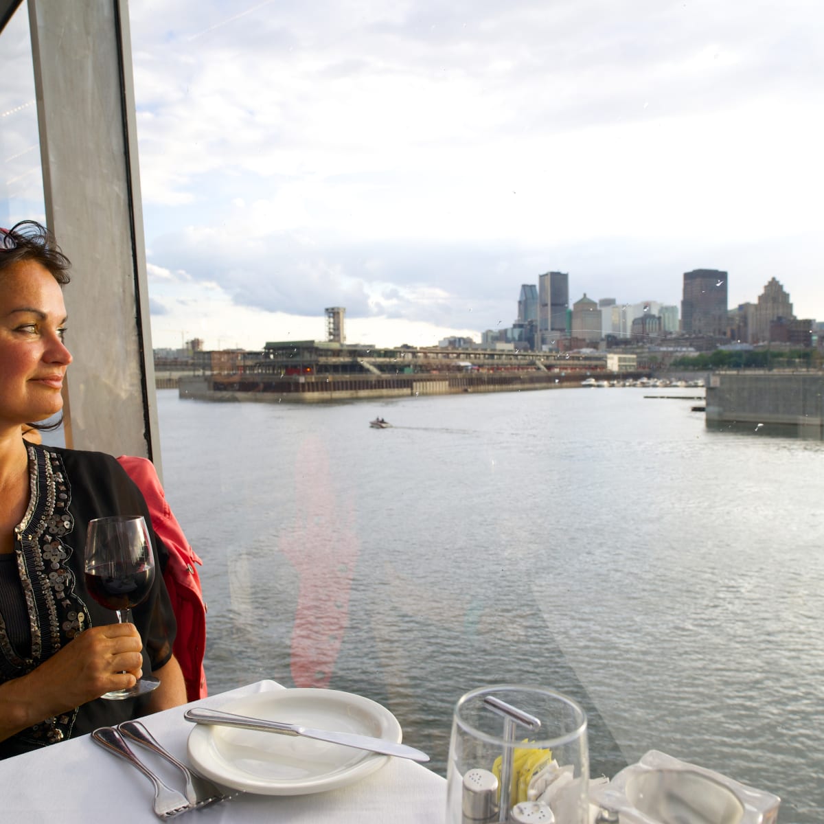 Woman on a cruise ship with a glass of wine admiring the view of Montreal.