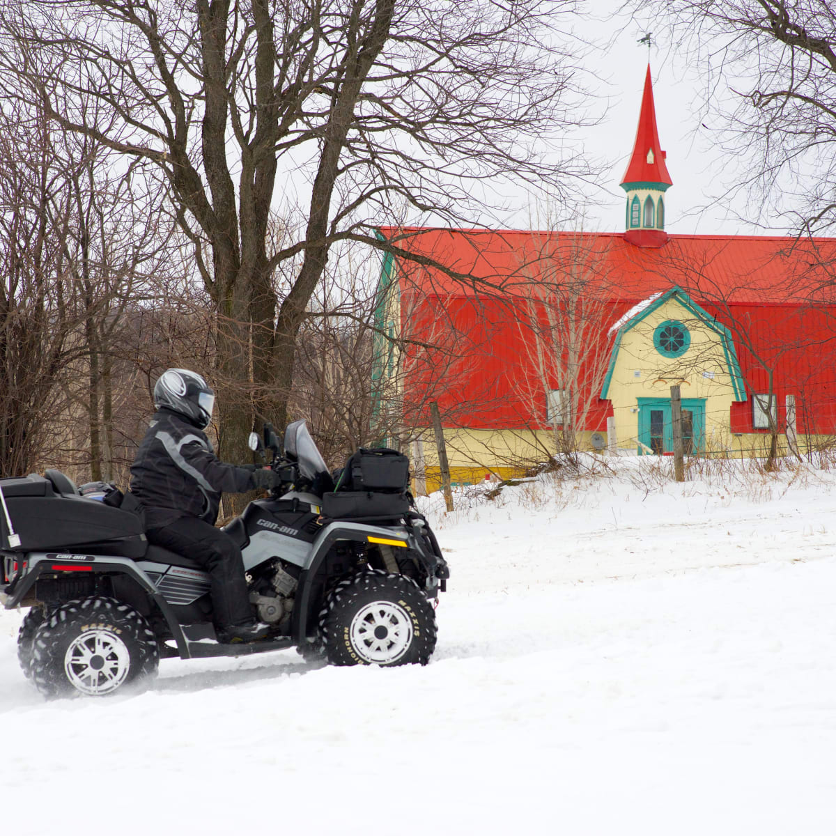 Quad rider in the snow in front of a heritage building.