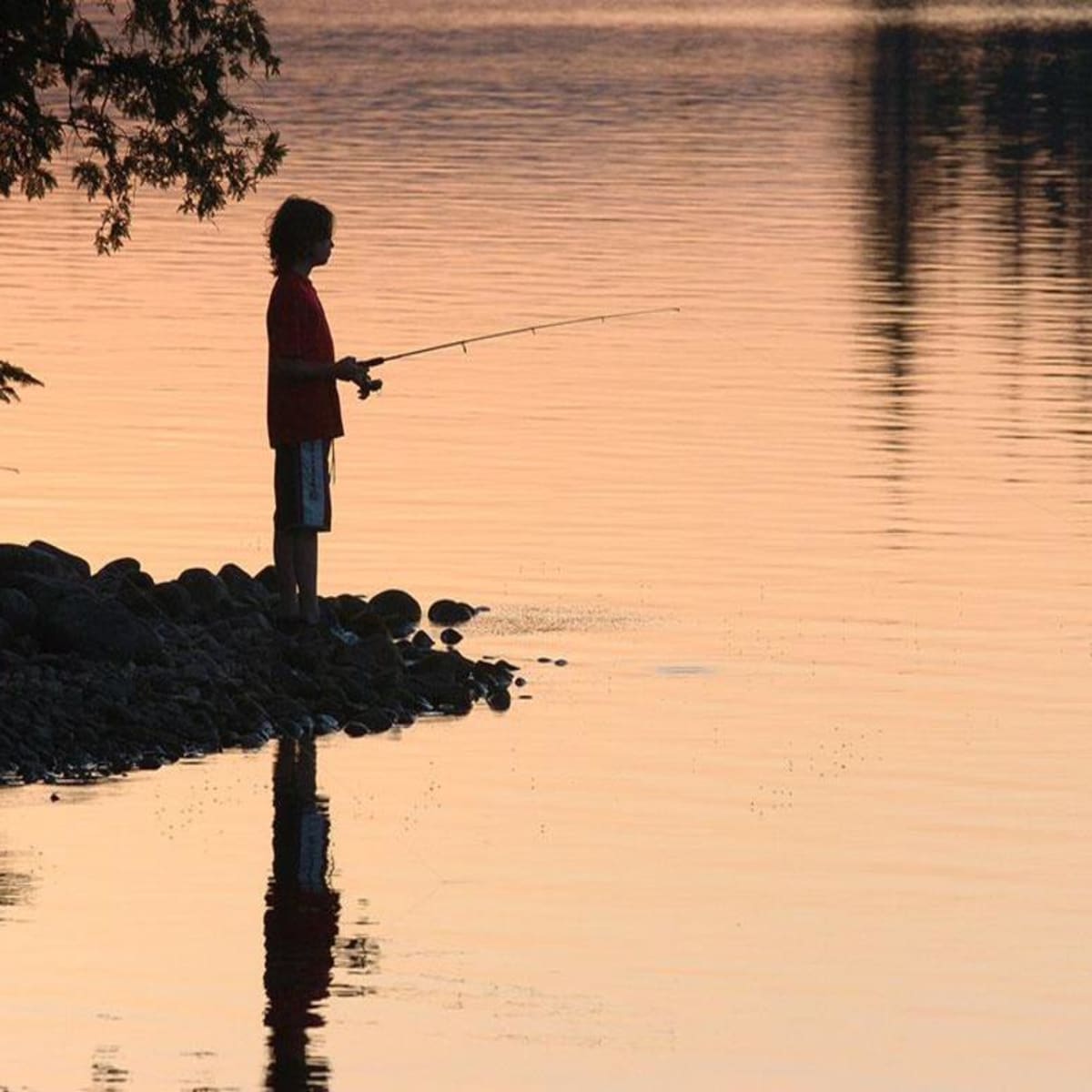 Garçon qui pêche au lac au coucher de soleil.