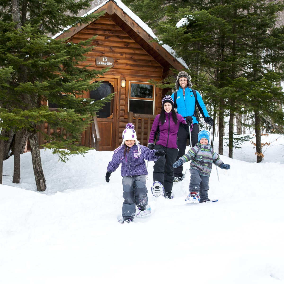 A family snowshoeing next to a cottage at Sommet Morin Heights.
