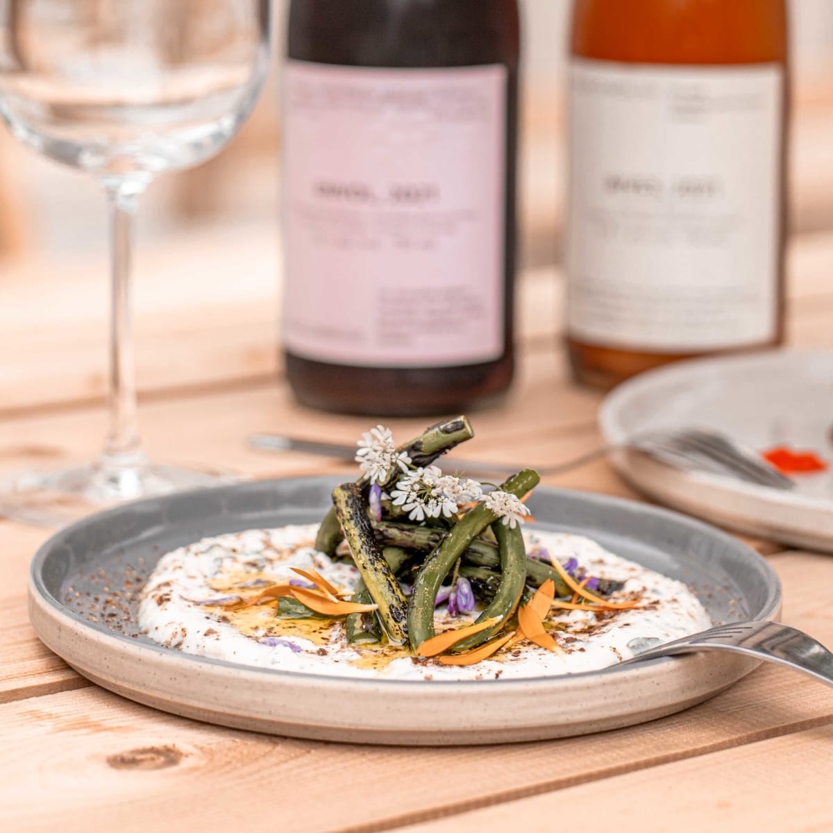 Gros plan sur une assiette soigneusement dressée, avec un verre à vin et deux bouteilles de vin en arrière-plan.