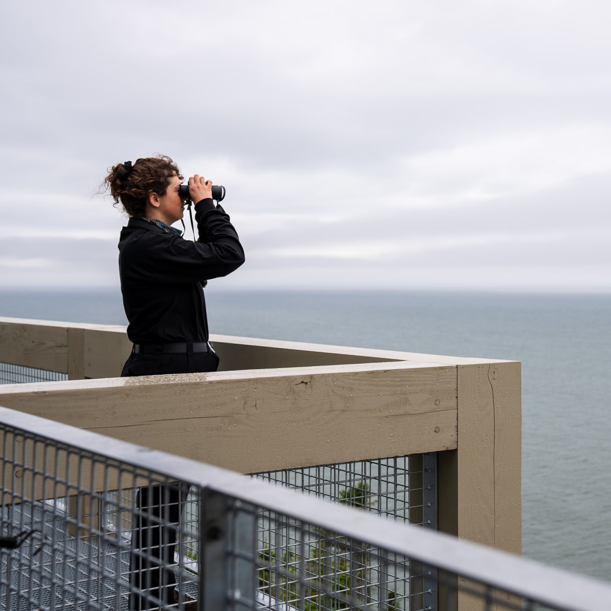 Woman, binoculars in hand, observing the horizon at the Putep’t-awt observation site.