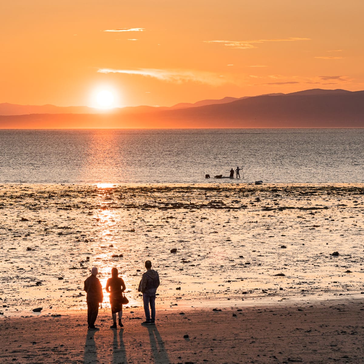 Trois personnes de dos sur le bord de l'eau regardant un couché de soleil.