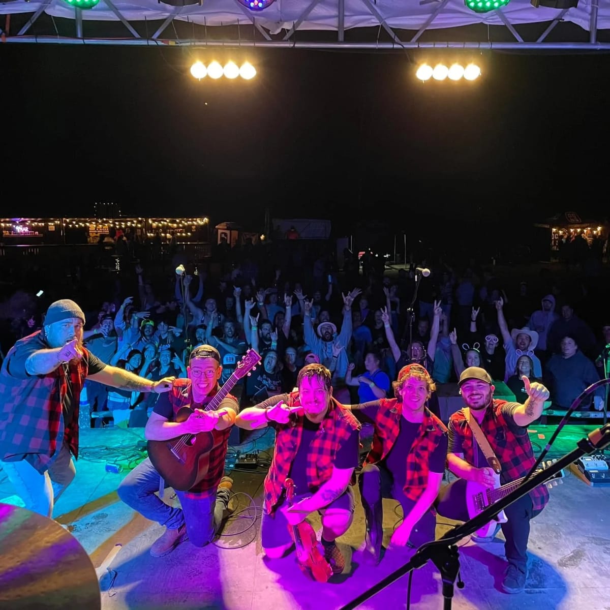 A group of musicians on stage being photographed in front of the crowd at a festival.