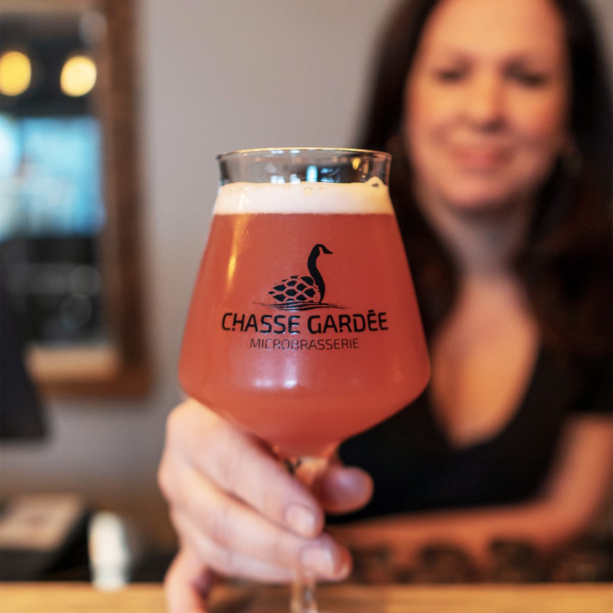 Microbrasserie La chasse gardée - Femme tenant une coupe de bière à l’effigie de la microbrasserie.