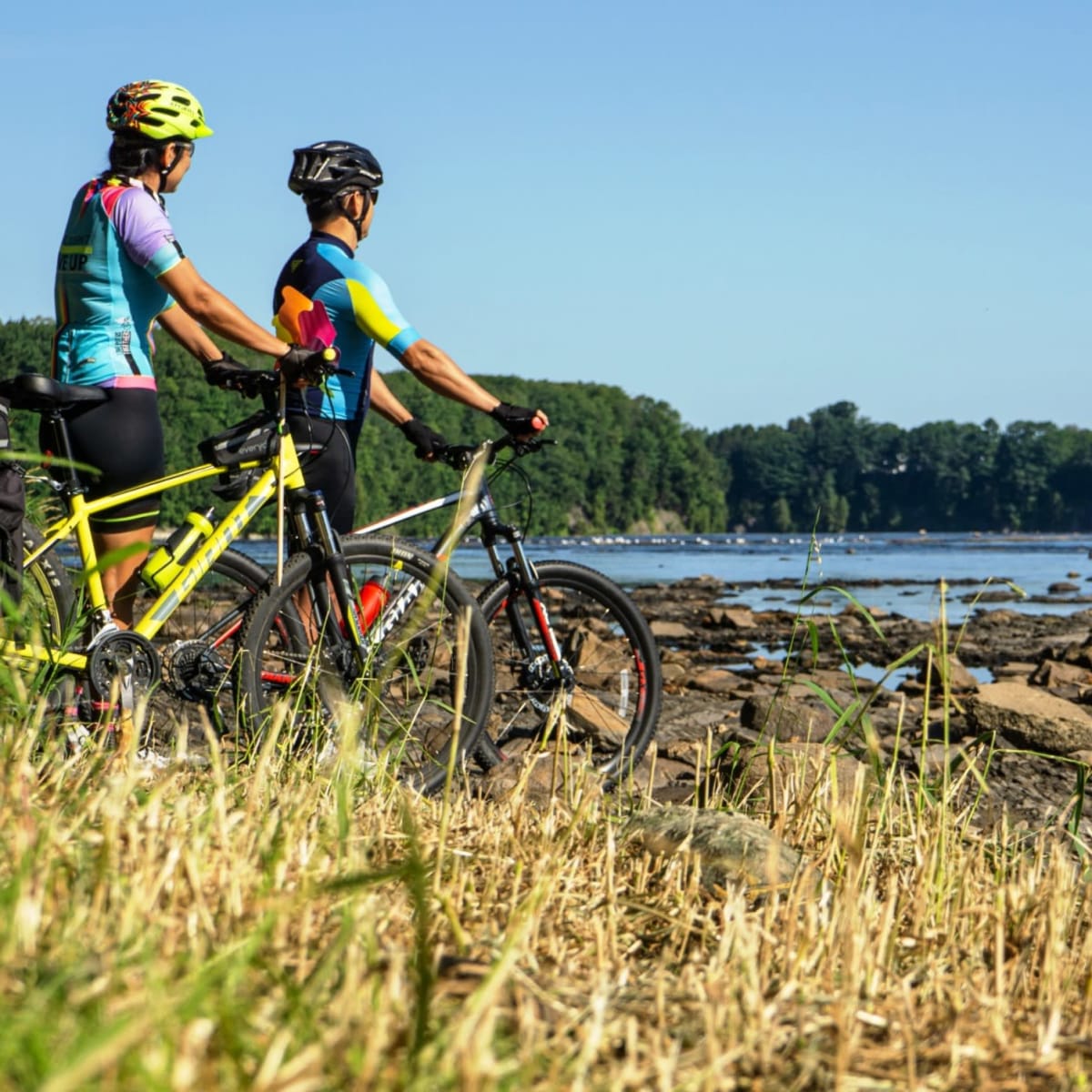A couple riding bicycles along a riverbank.